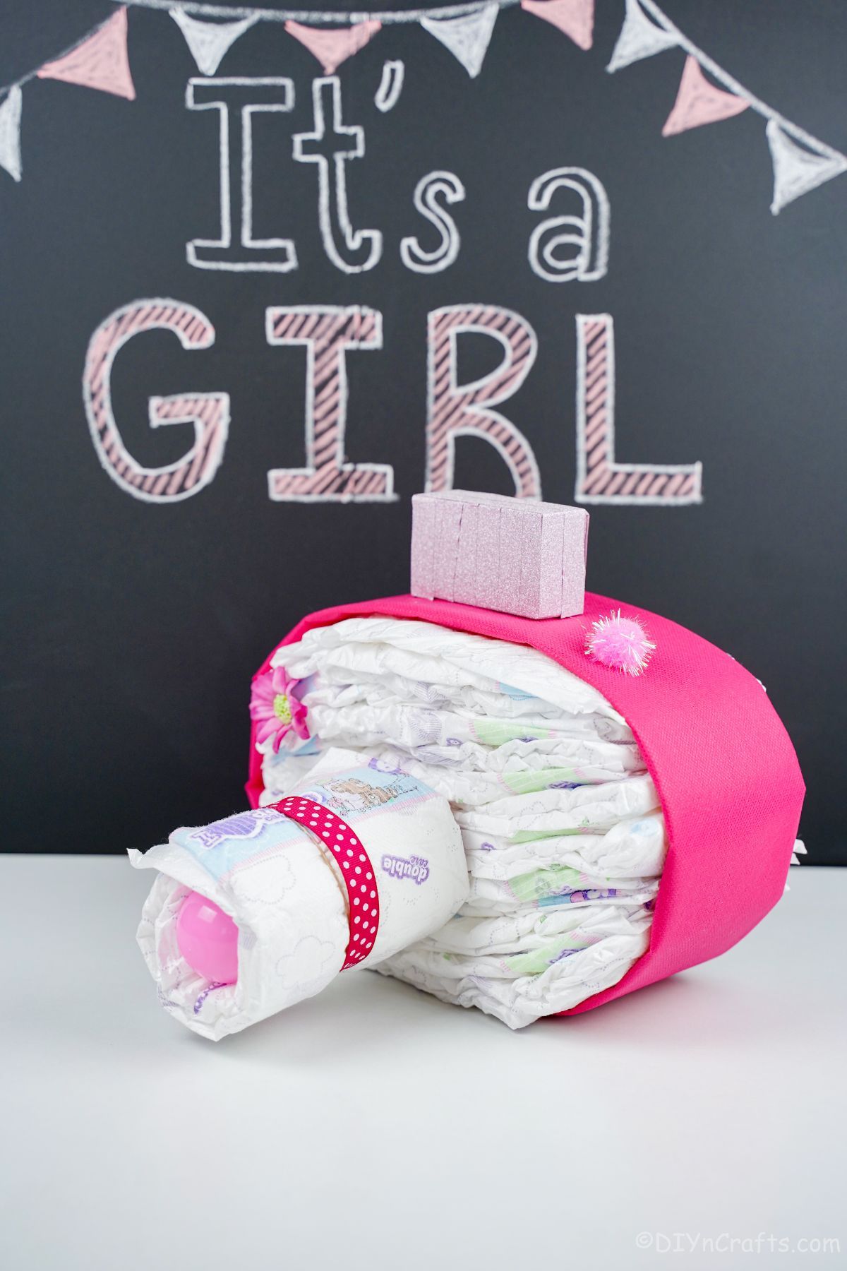 pink camera diaper cake on white table with chalkboard in background