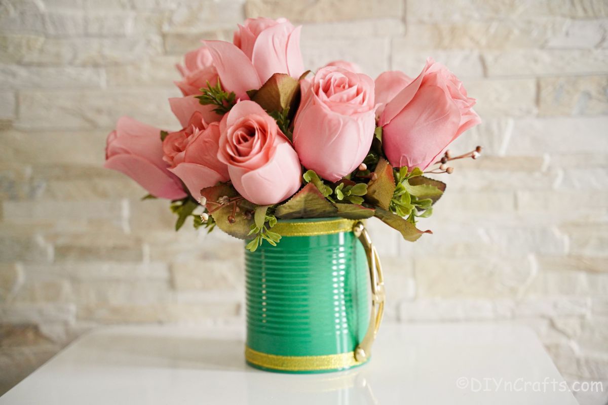 pink roses in green tin can with gold handle on white table