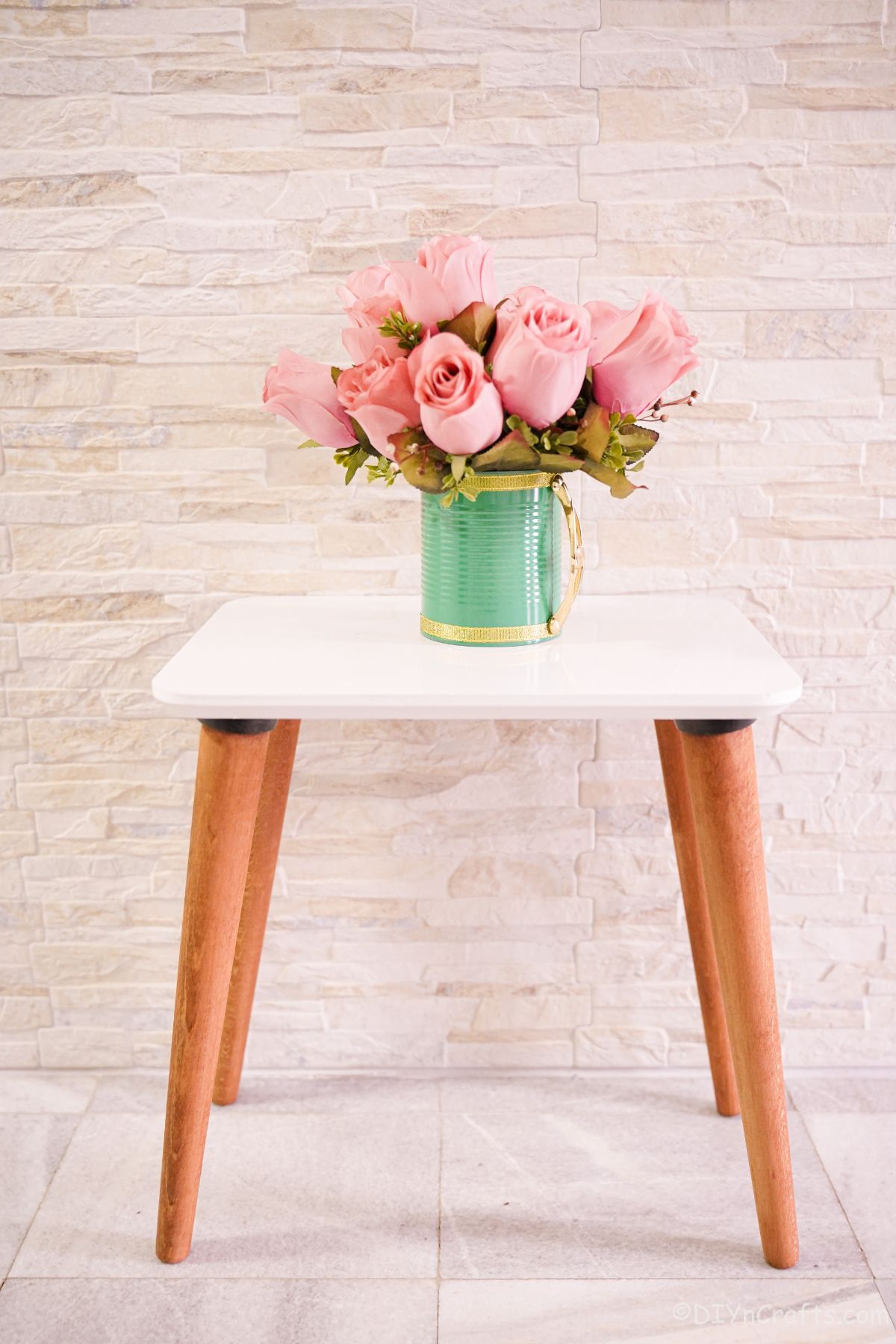 green mug vase holding pink flowers sitting on white end table