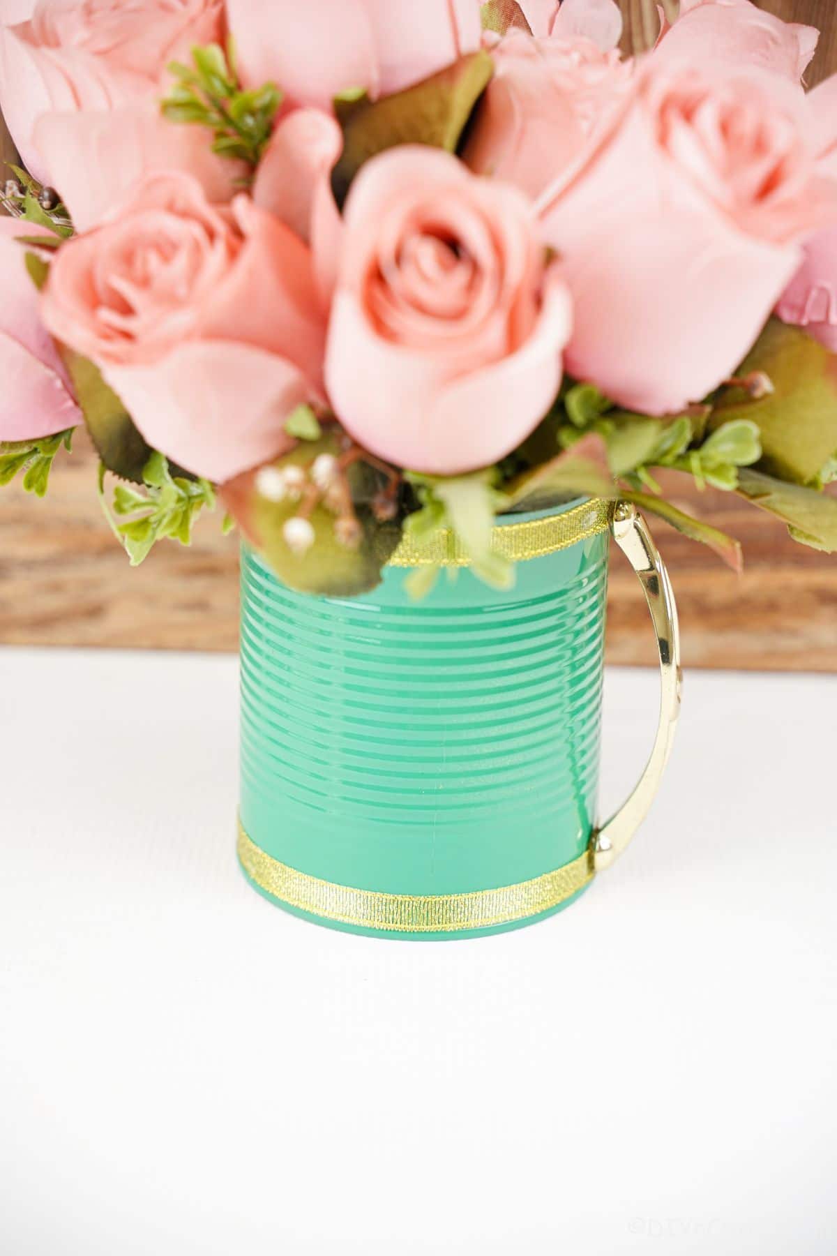 green tin can with gold edge and pink flowers on white table