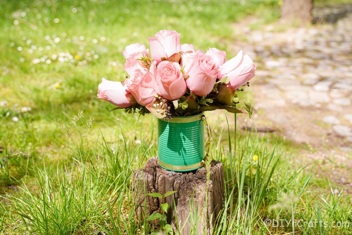 green tin can with gold trim on stump with pink roses