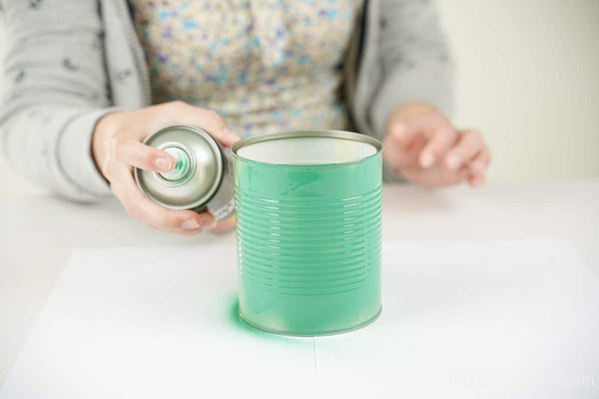 hand spraying green paint on tin can