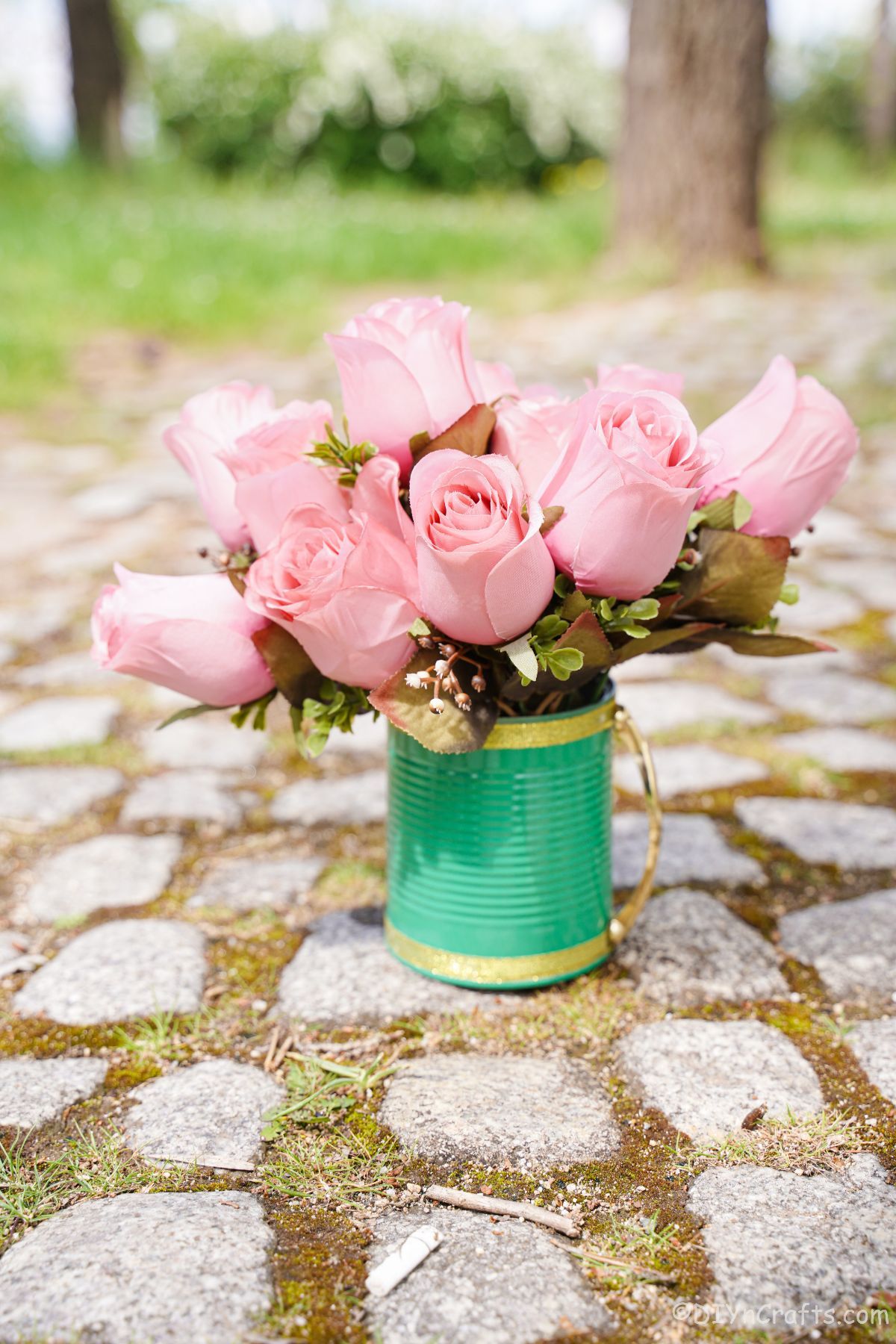 pink roses inside green mug on rock path