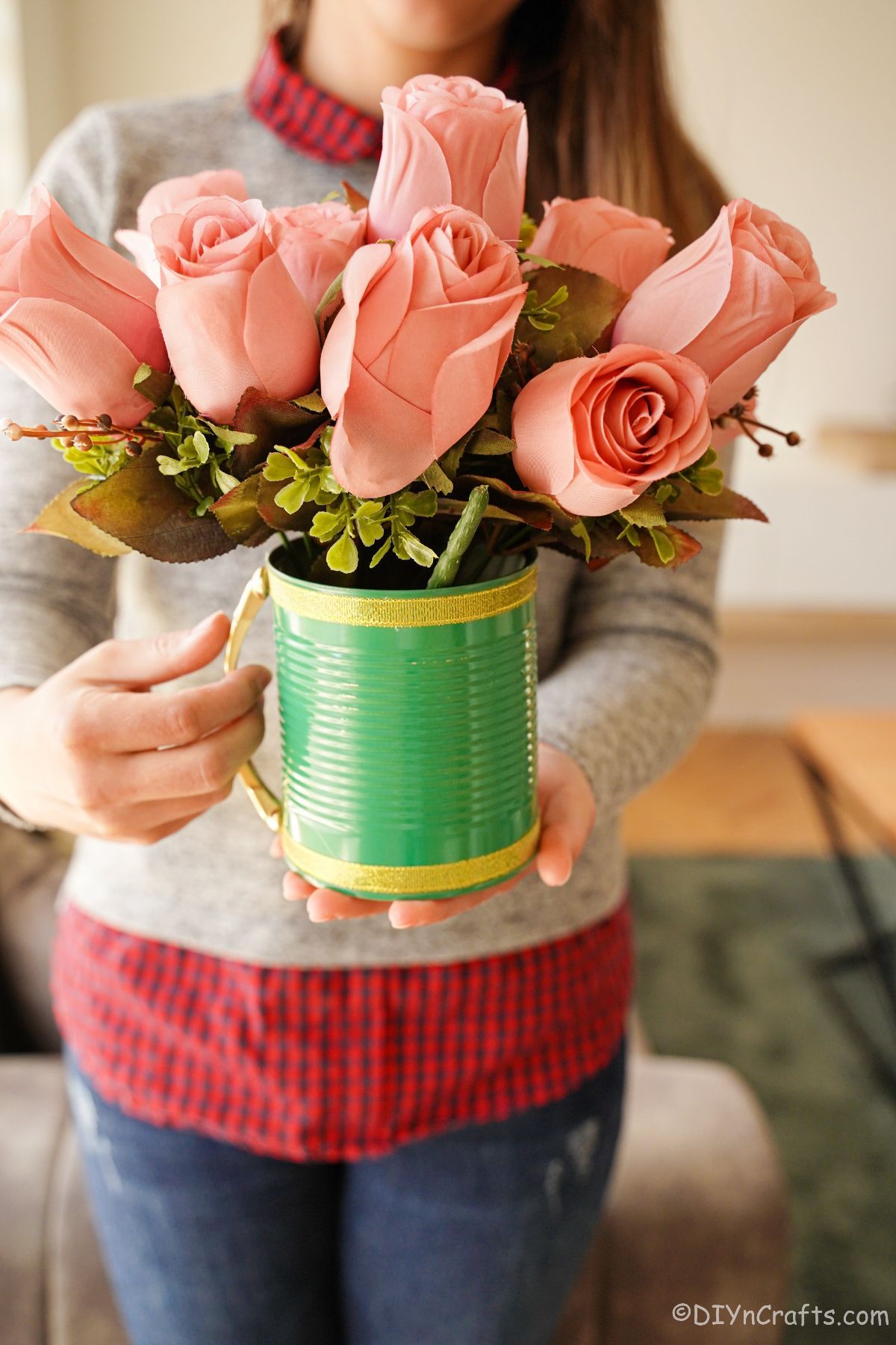 lady in grey sweater with red plaid shirt holding green tin can with pink flowers