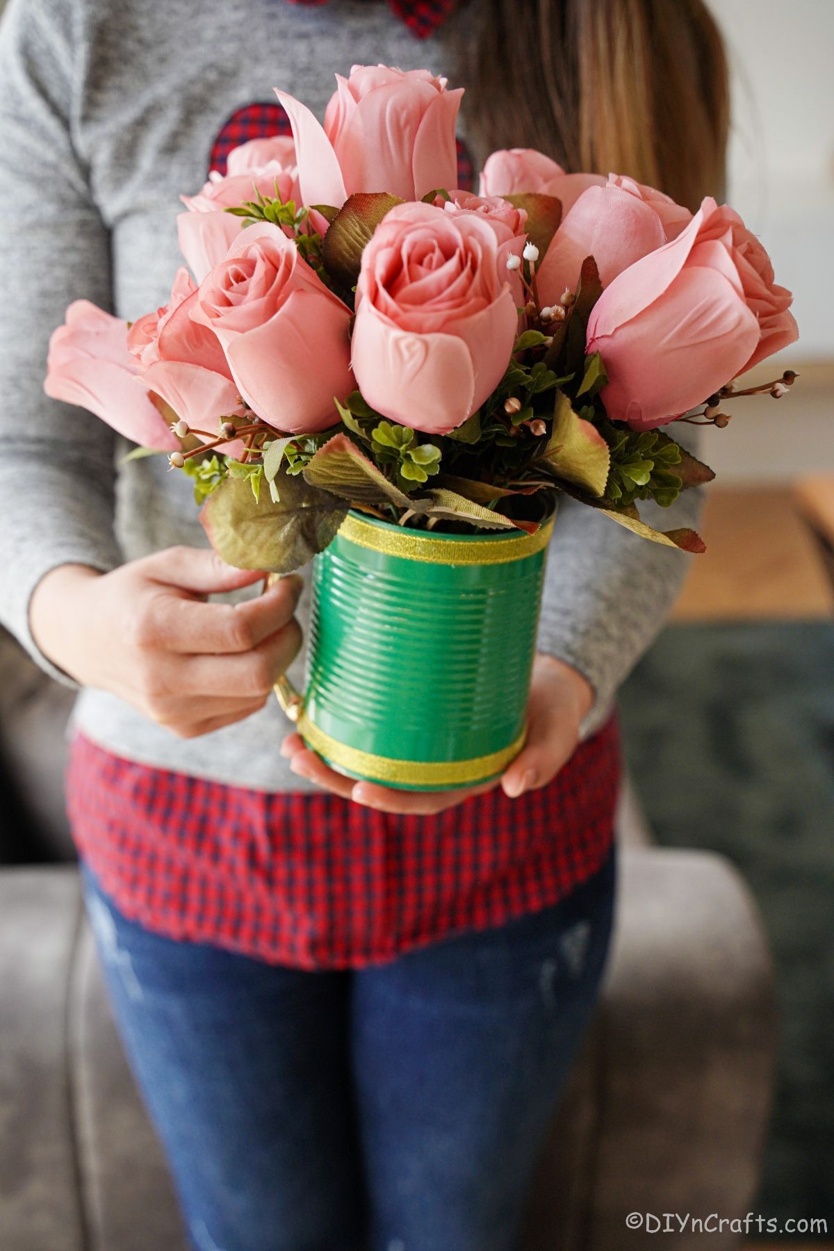 pink roses in green mug held by lady in grey and red