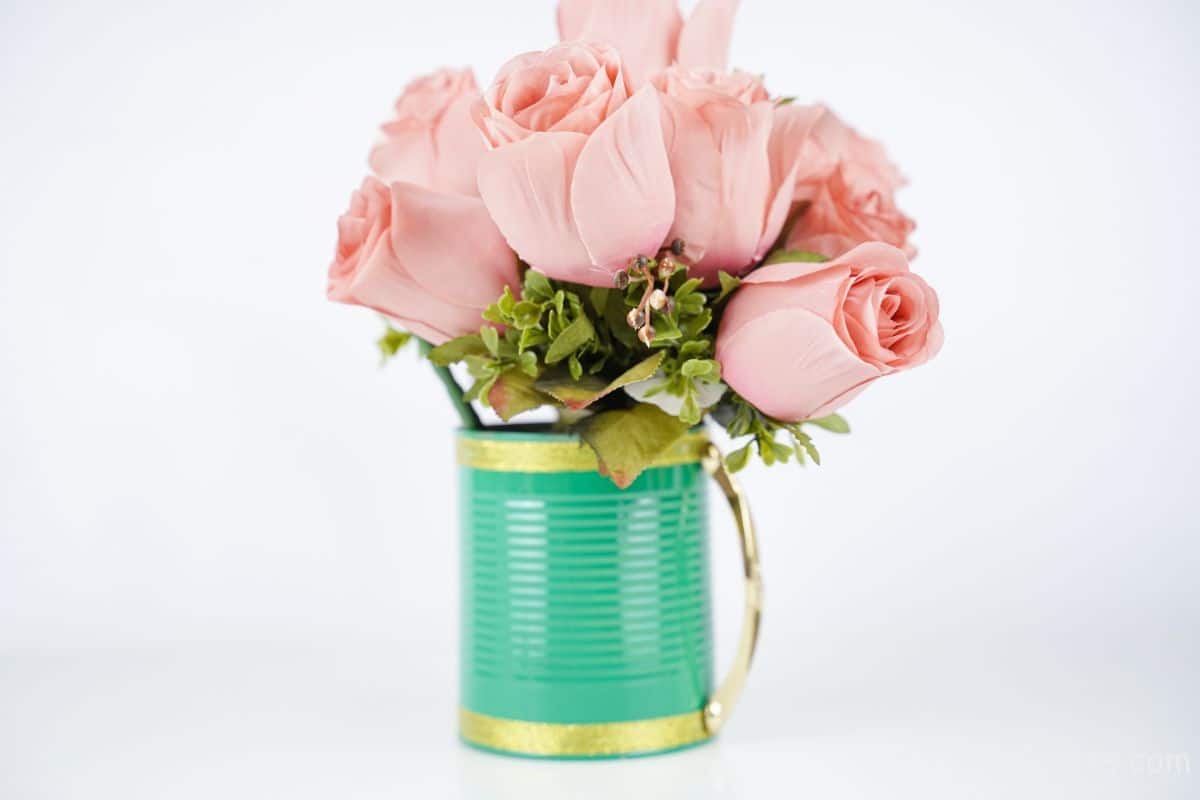 light green and gold tin can with gold handle on white table holding pink roses