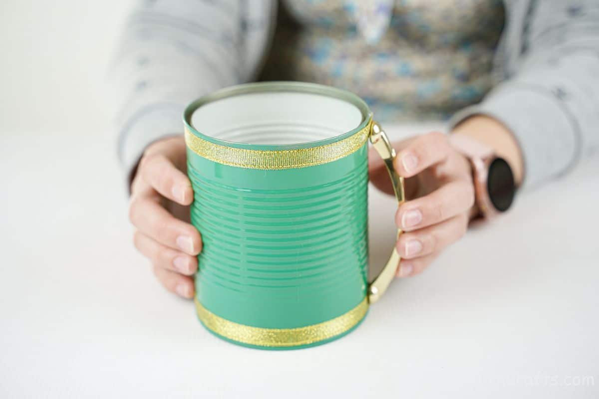 hand holding gold handle on side of green tin can