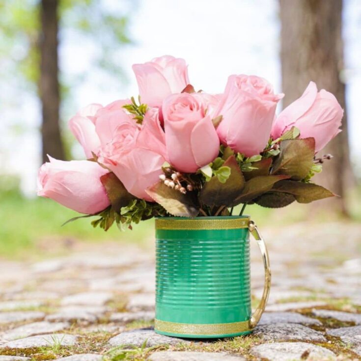 green tin can with pink roses on cobblestones