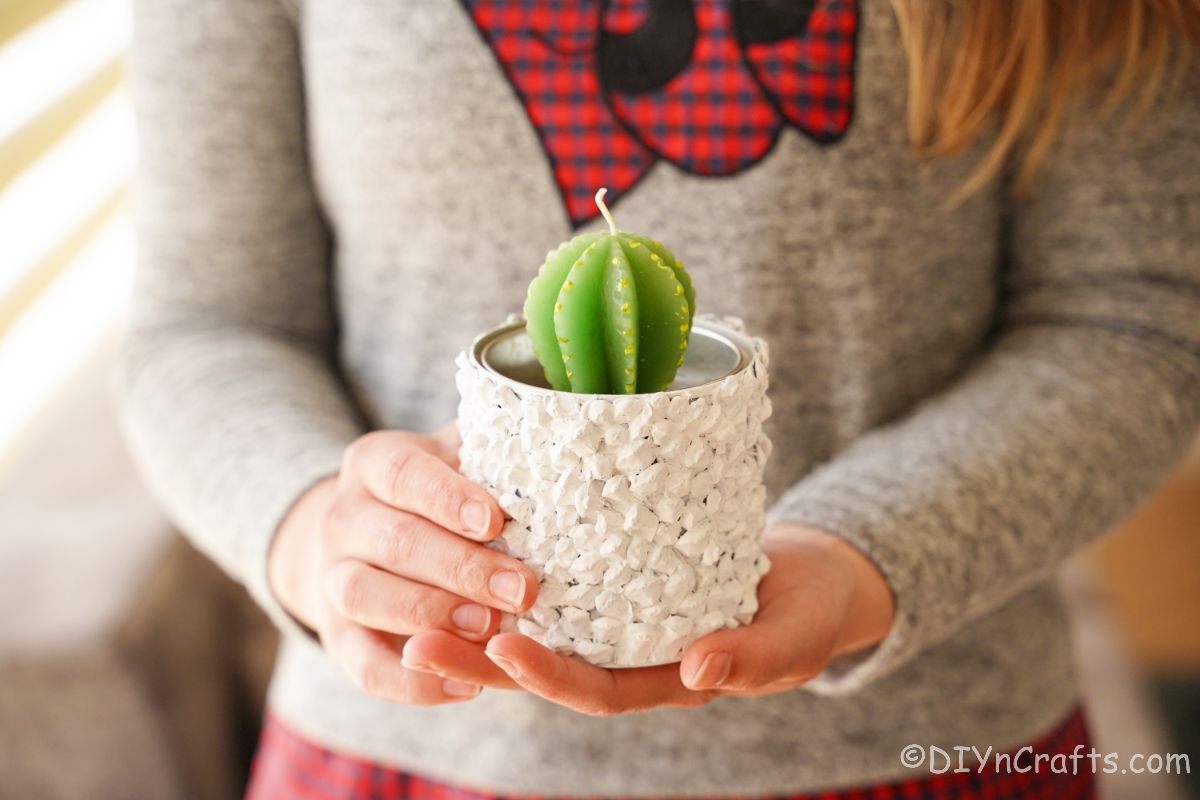 white planter holding green candle held by lady in grey and red sweater