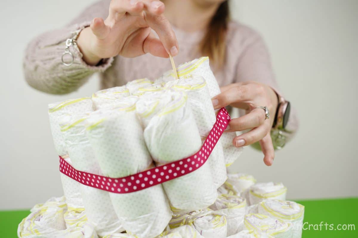 hand adding dowel through diapers on diaper cake