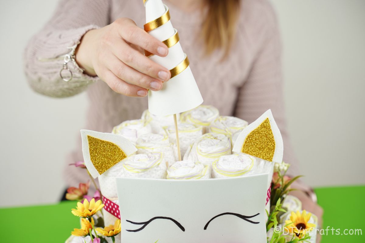 lady adding unicorn horn to diaper cake