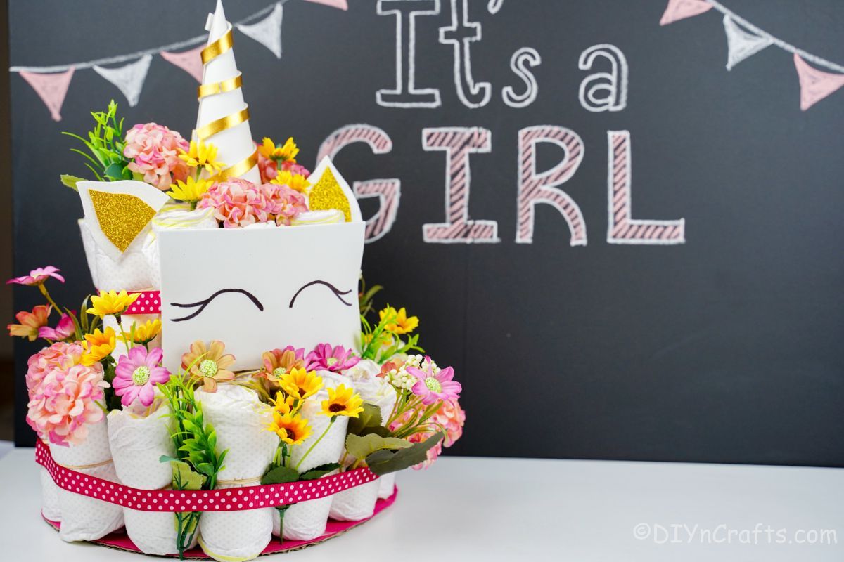 unicorn diaper cake in front of chalkboard sign that says its a girl