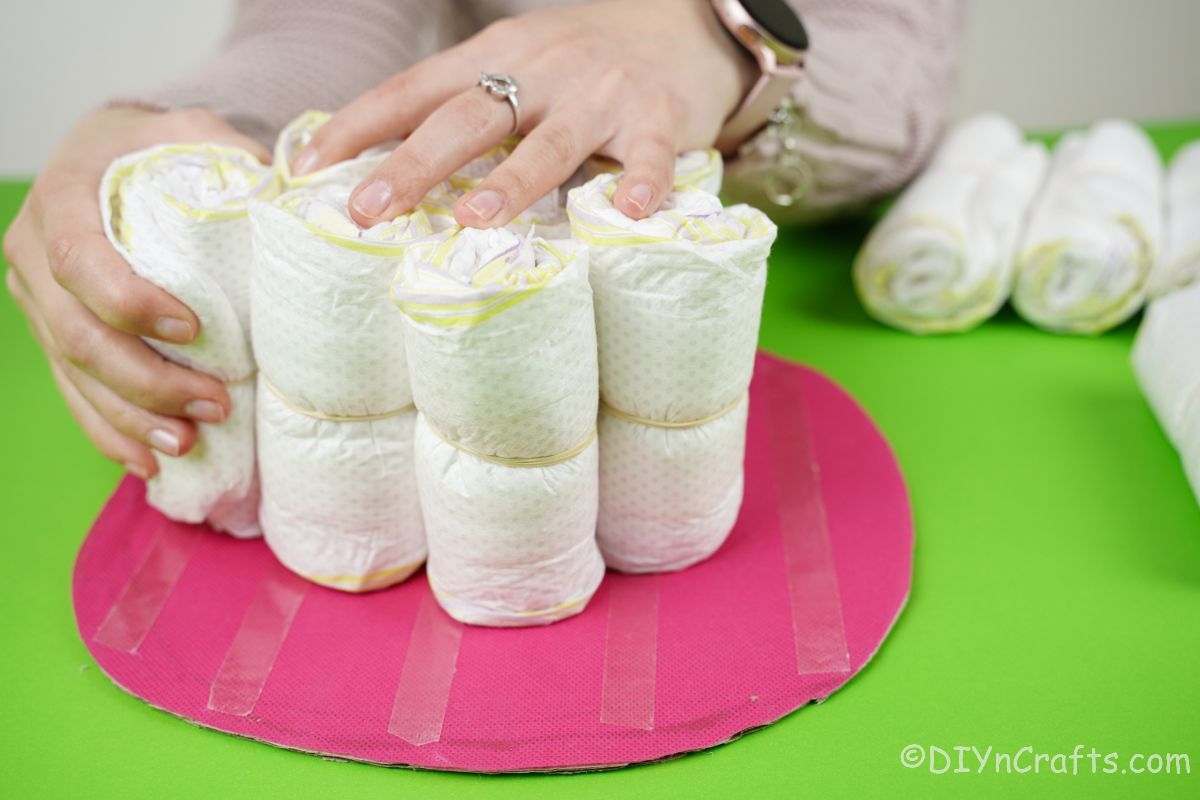 hand placing diaper rolls onto pink base