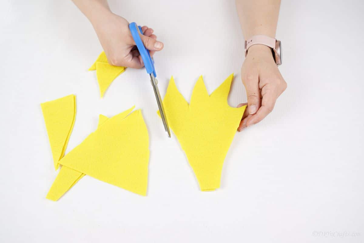 hand holding blue scissors to cut flame out of yellow felt