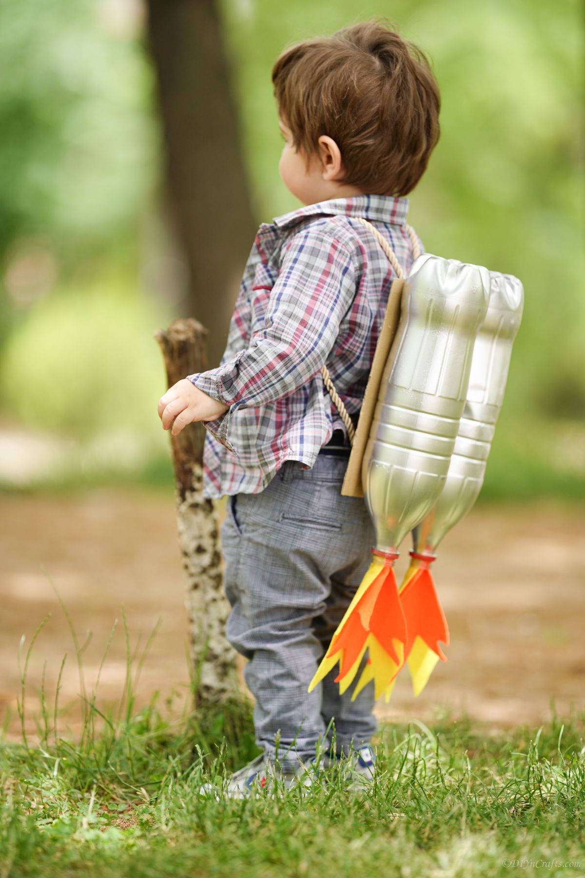brown haired toddler boy standing on grass wearing jet pack costume