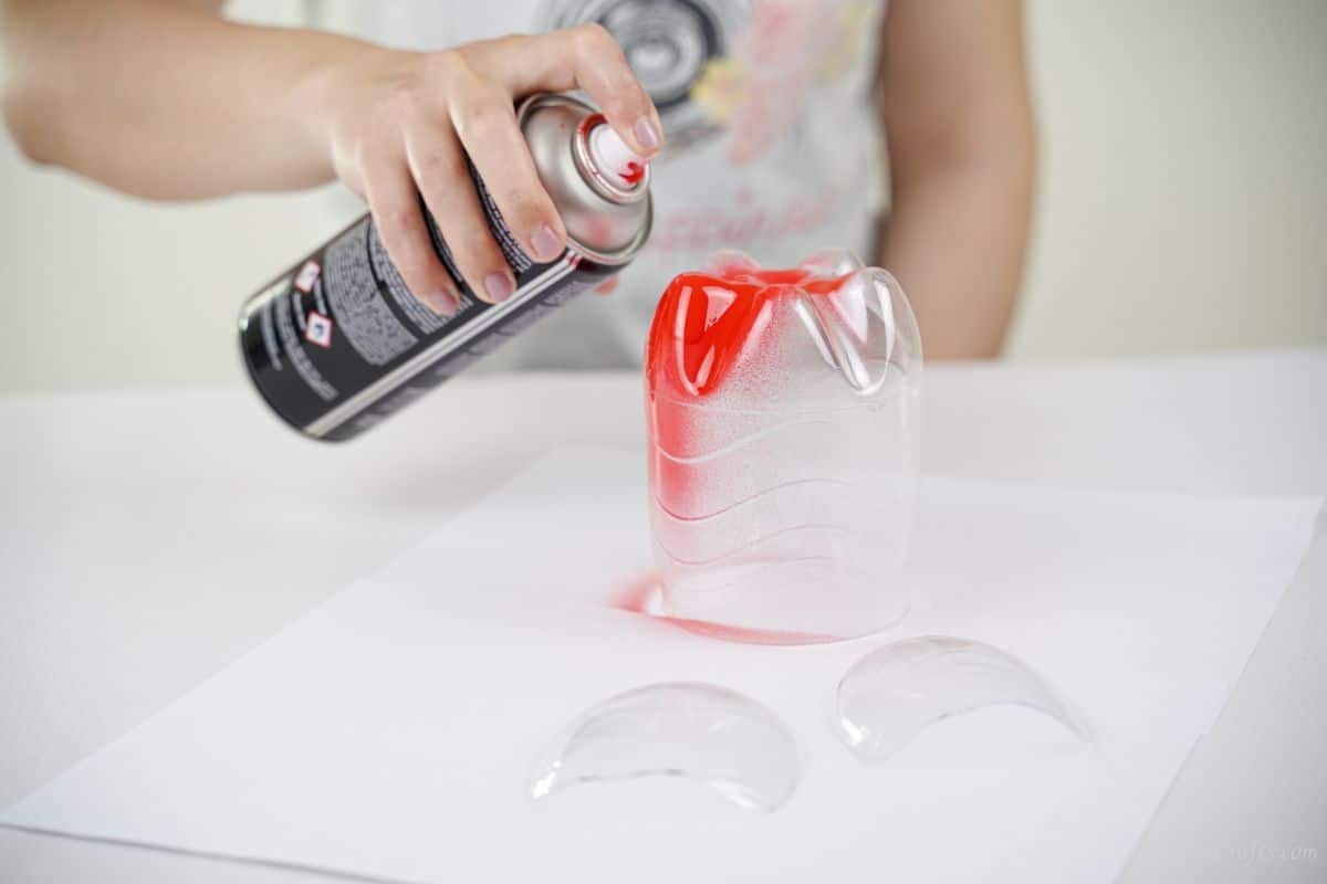 hand spraying plastic bottle pieces with red spray paint