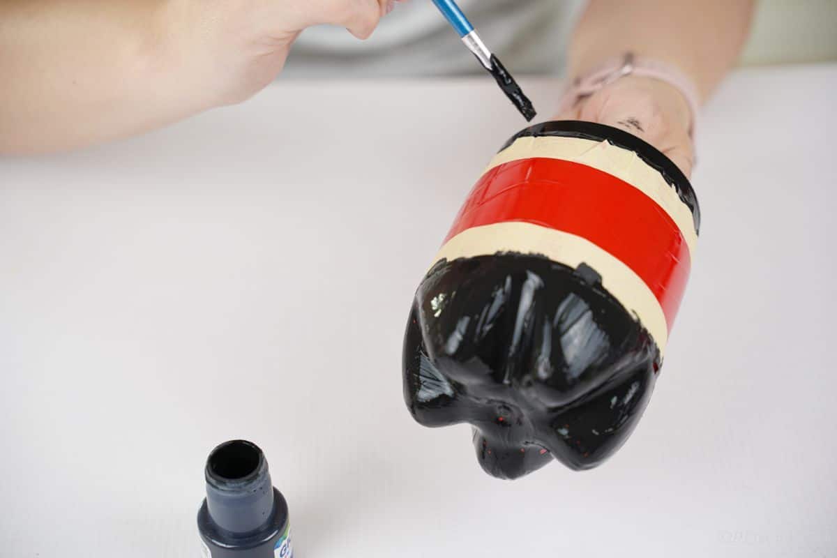 hand painting black paint above tape line on bottle