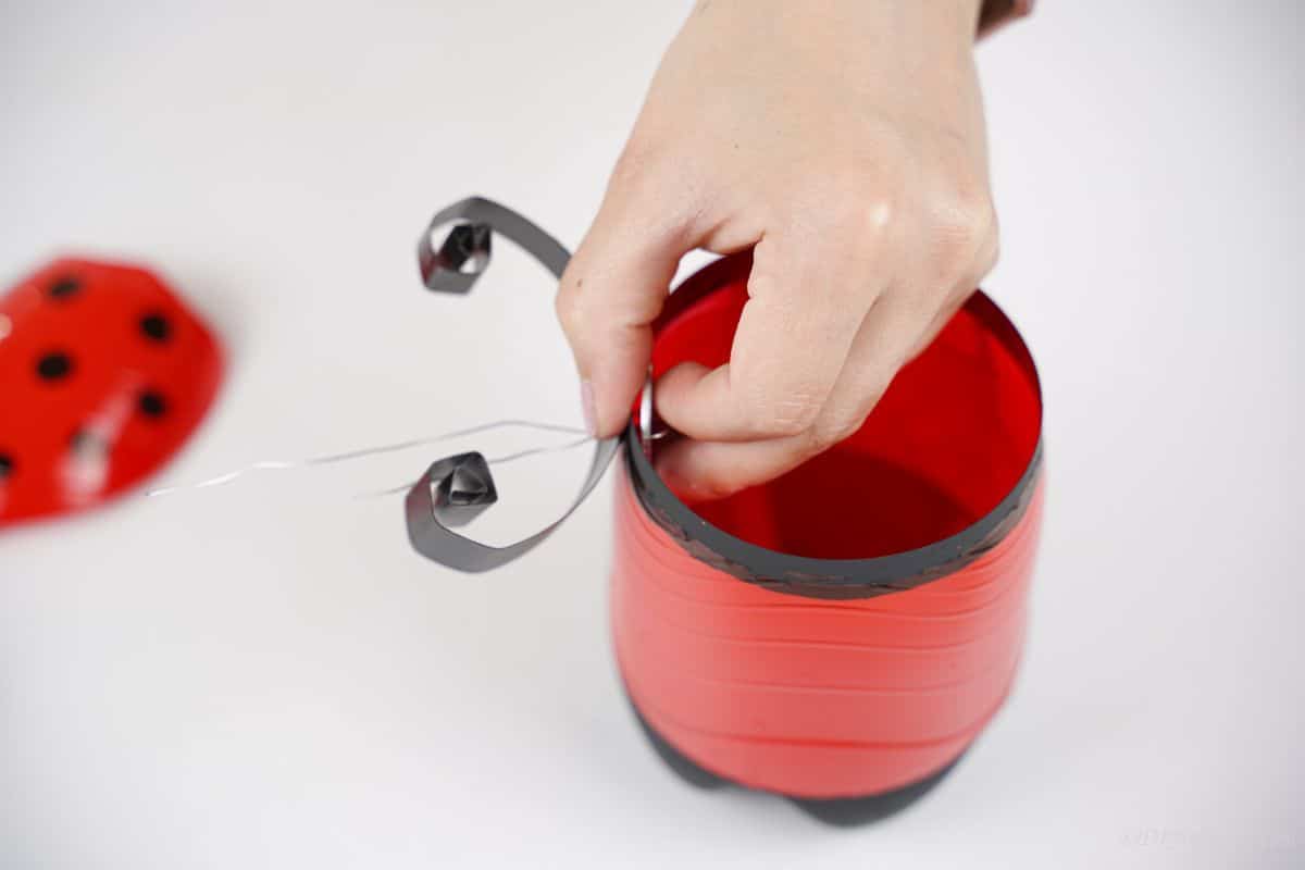 hand attaching antenna to red ladybug bottle