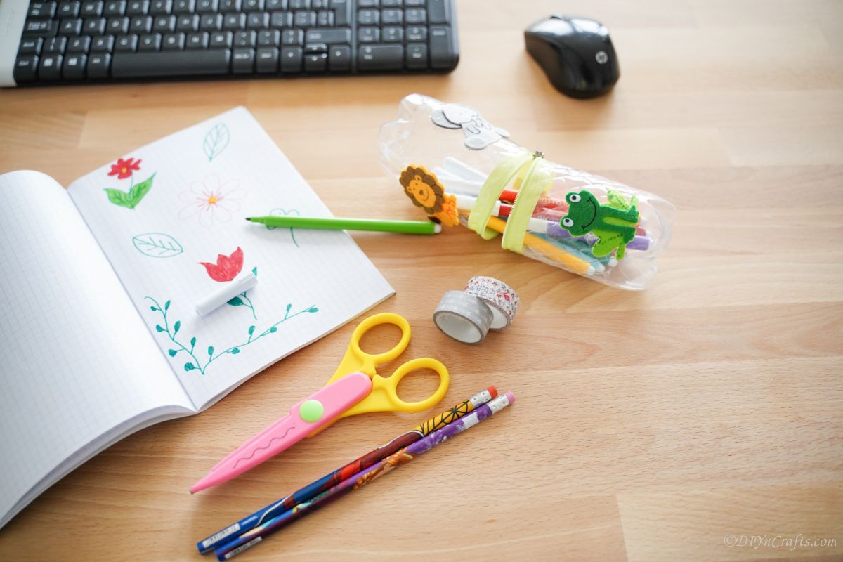plastic bottle pencil case on desk next to scissors pencils and keyboard