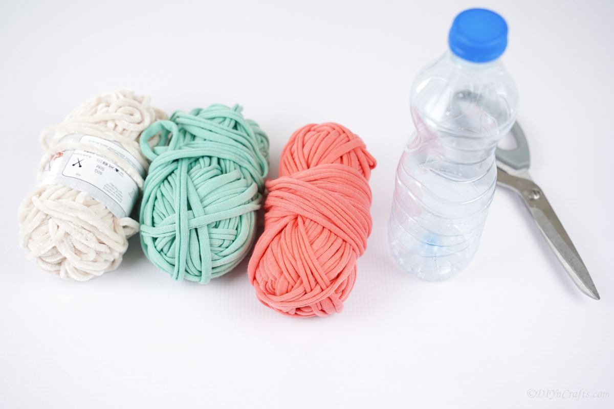 pink green white yarn with plastic bottle and scissors on white table