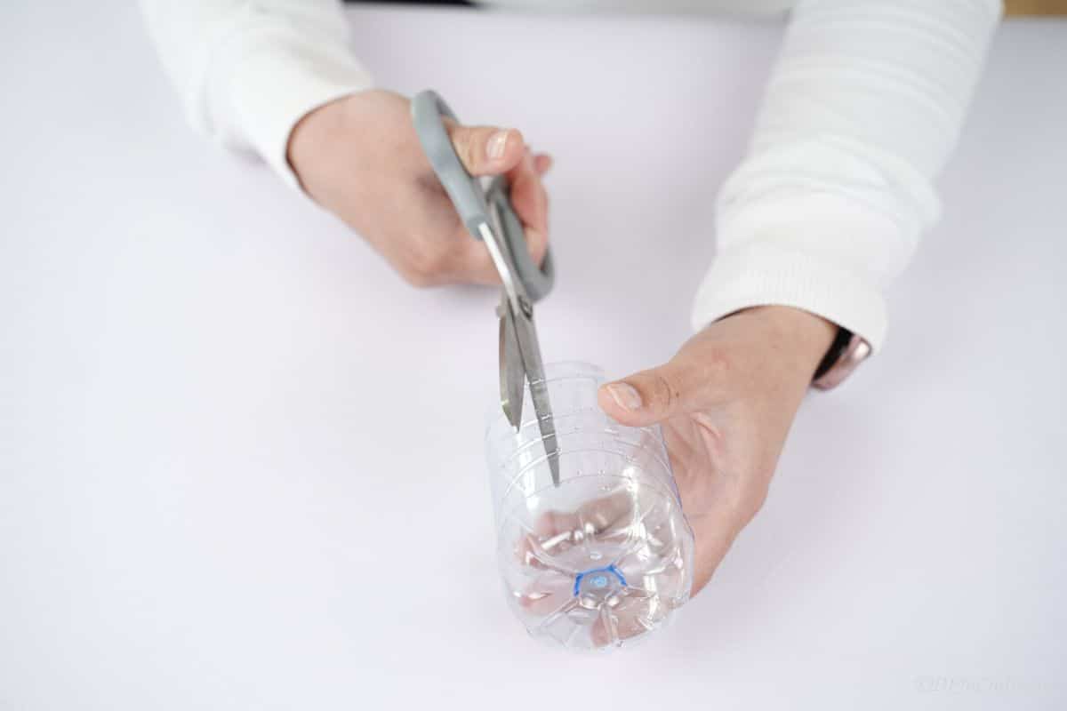 gray scissors cutting the sides of the plastic bottle