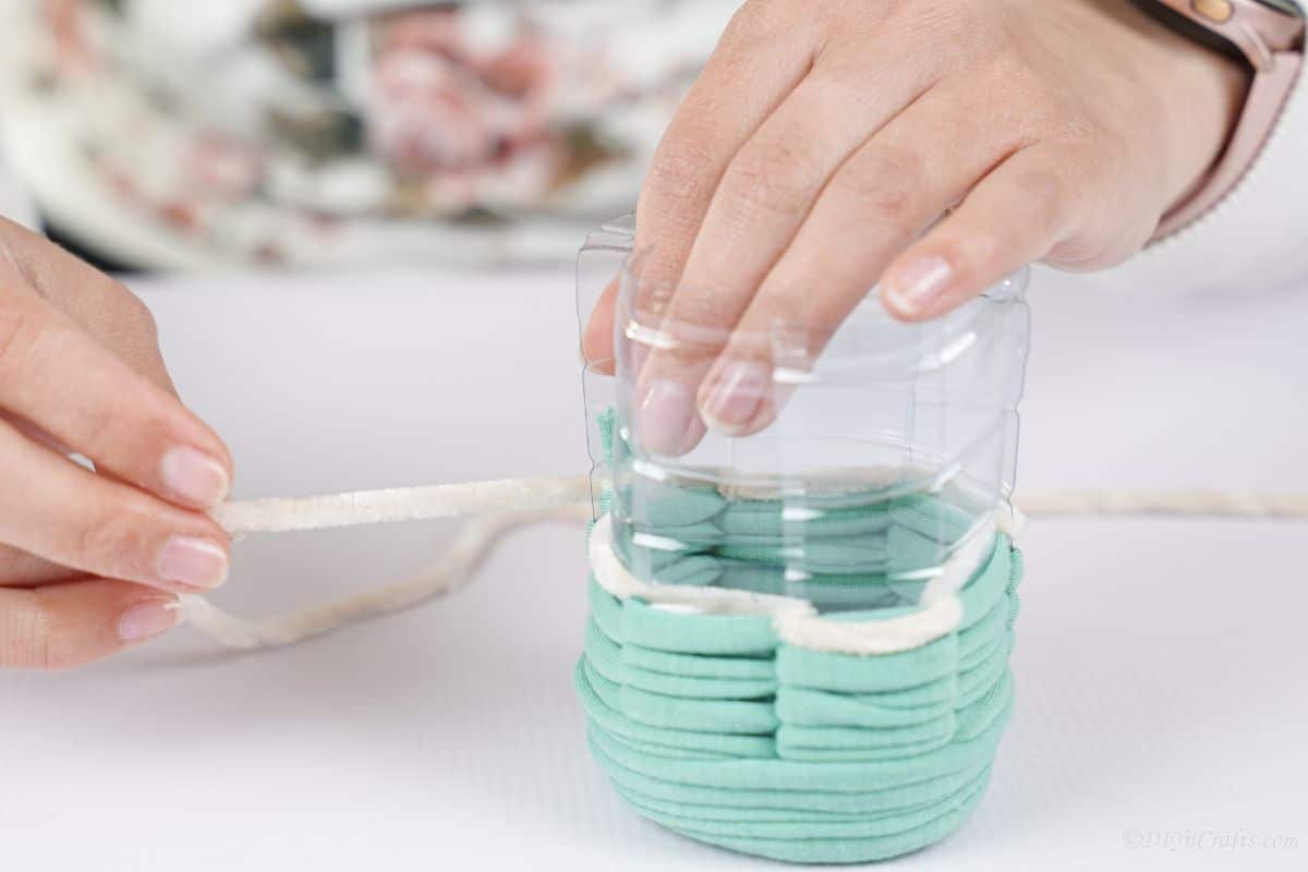 tying white and green yarn together on plastic cup