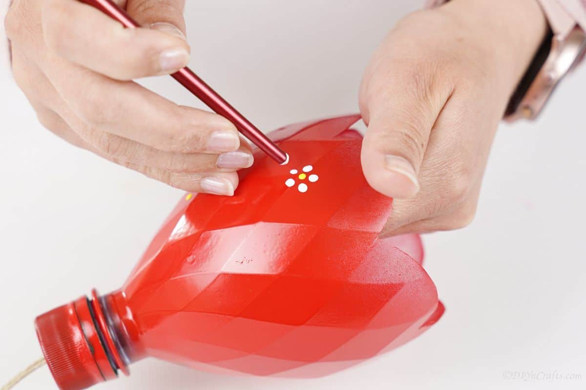 hand painting flowers onto red part of bottle