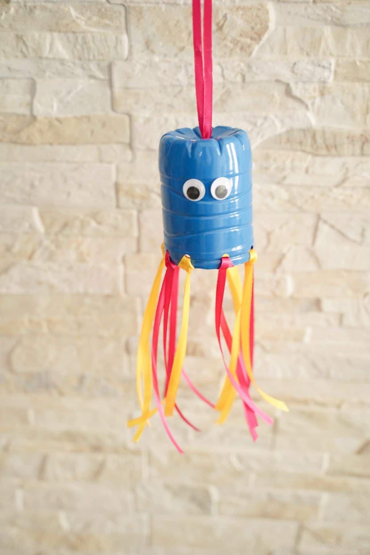 blue pink and yellow plastic bottle windsock against cream brick wall