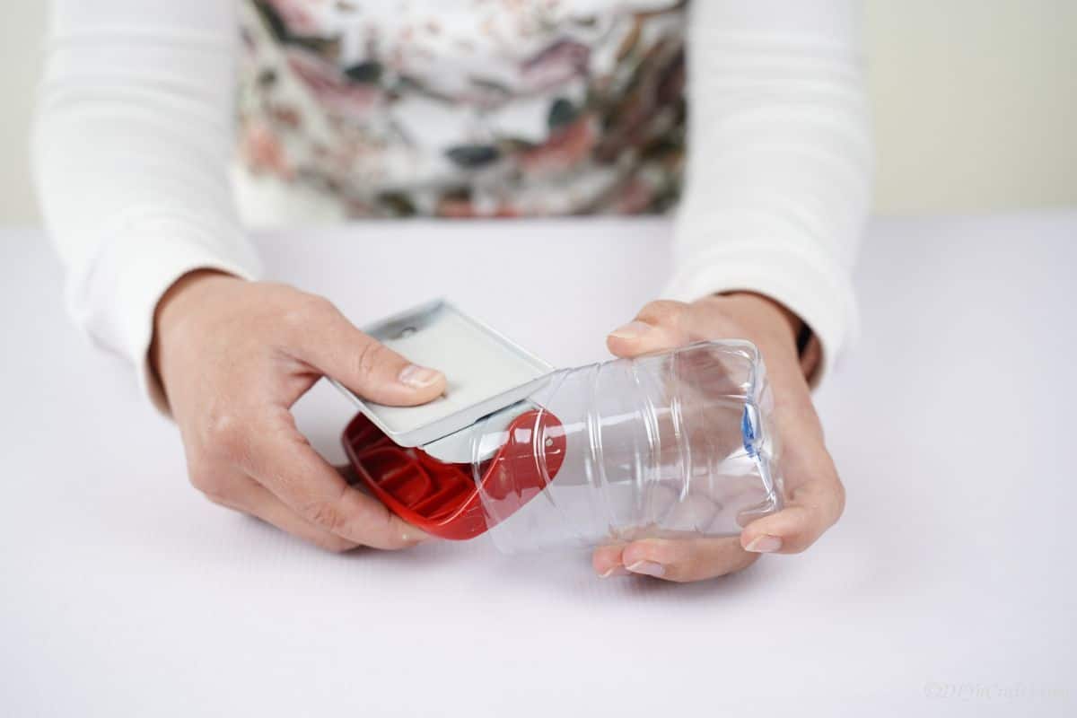 hand using the hole punch in the plastic bottle