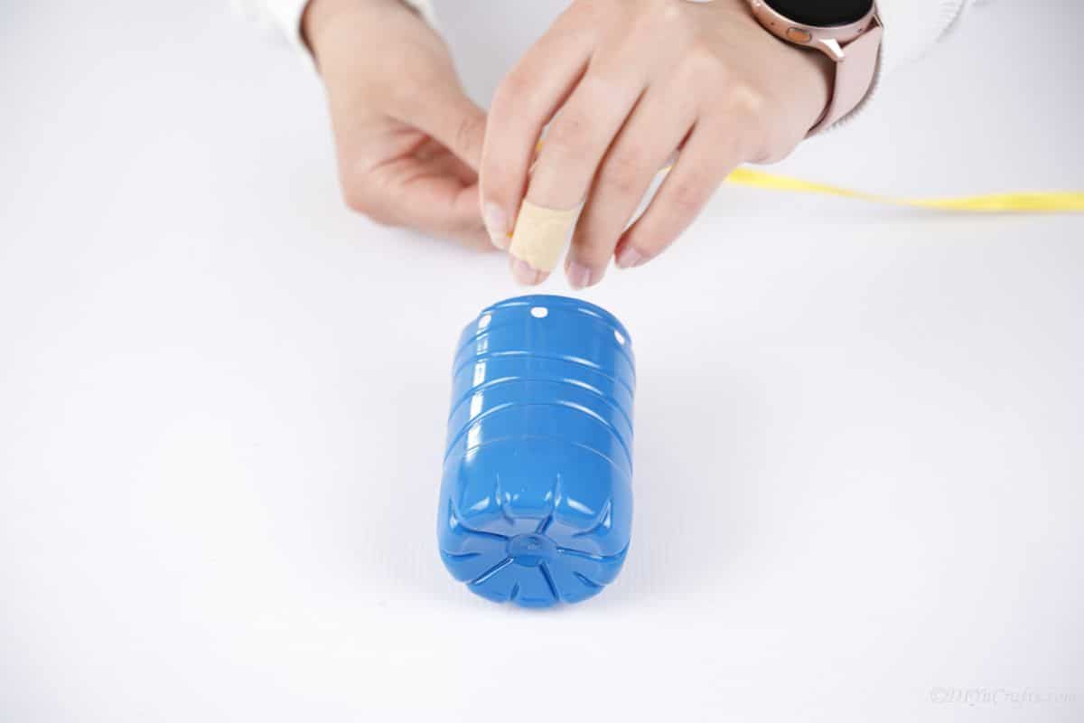 hand tying yellow ribbon on bottom of blue bottle