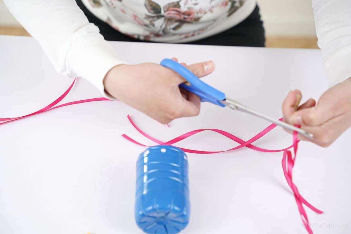 hand holding blue scissors cutting pink ribbon