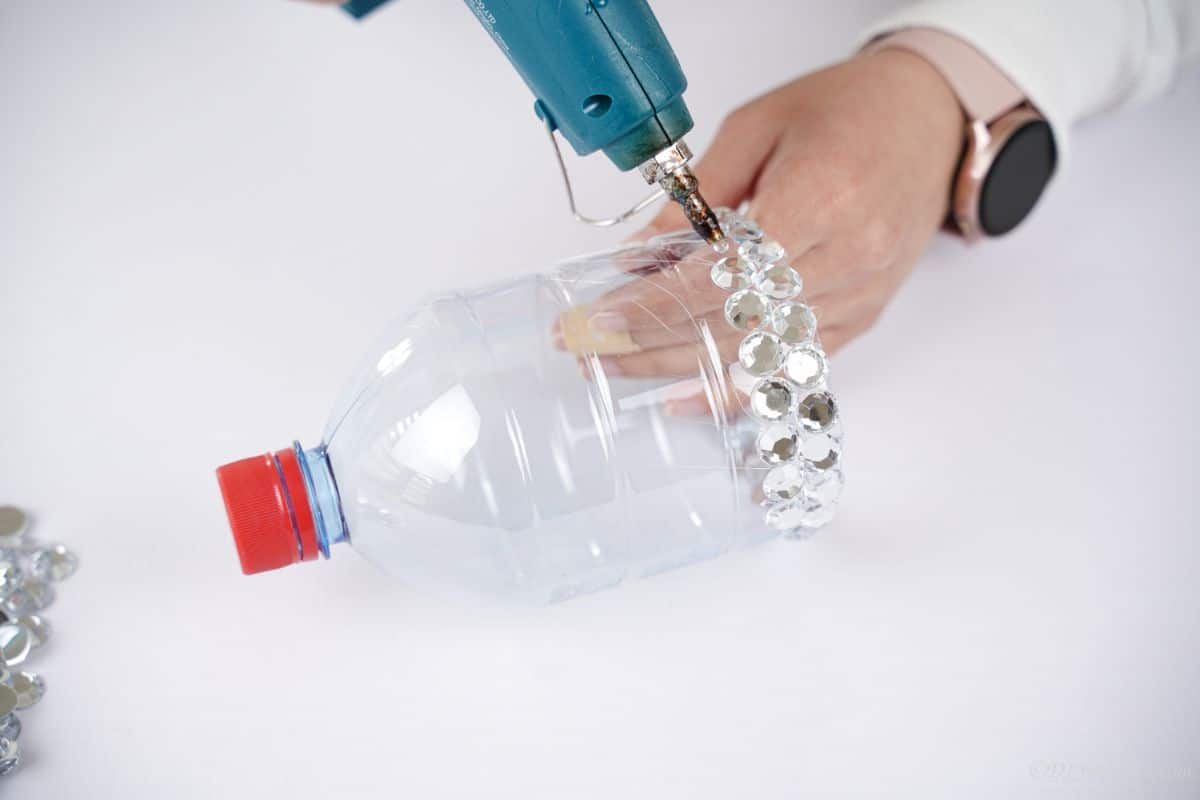 hand holding glue gun to attach more rhinestones onto plastic bottle