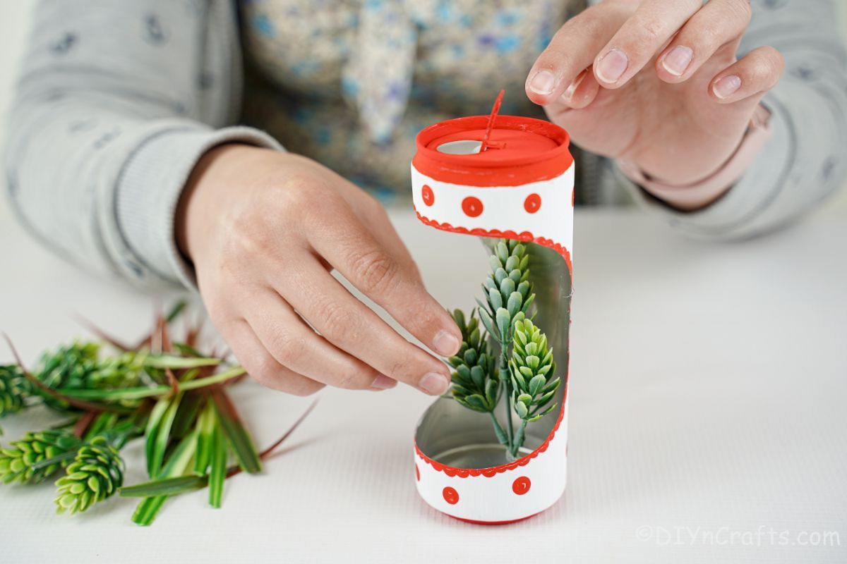 hand gluing fake greenery into soda can planter