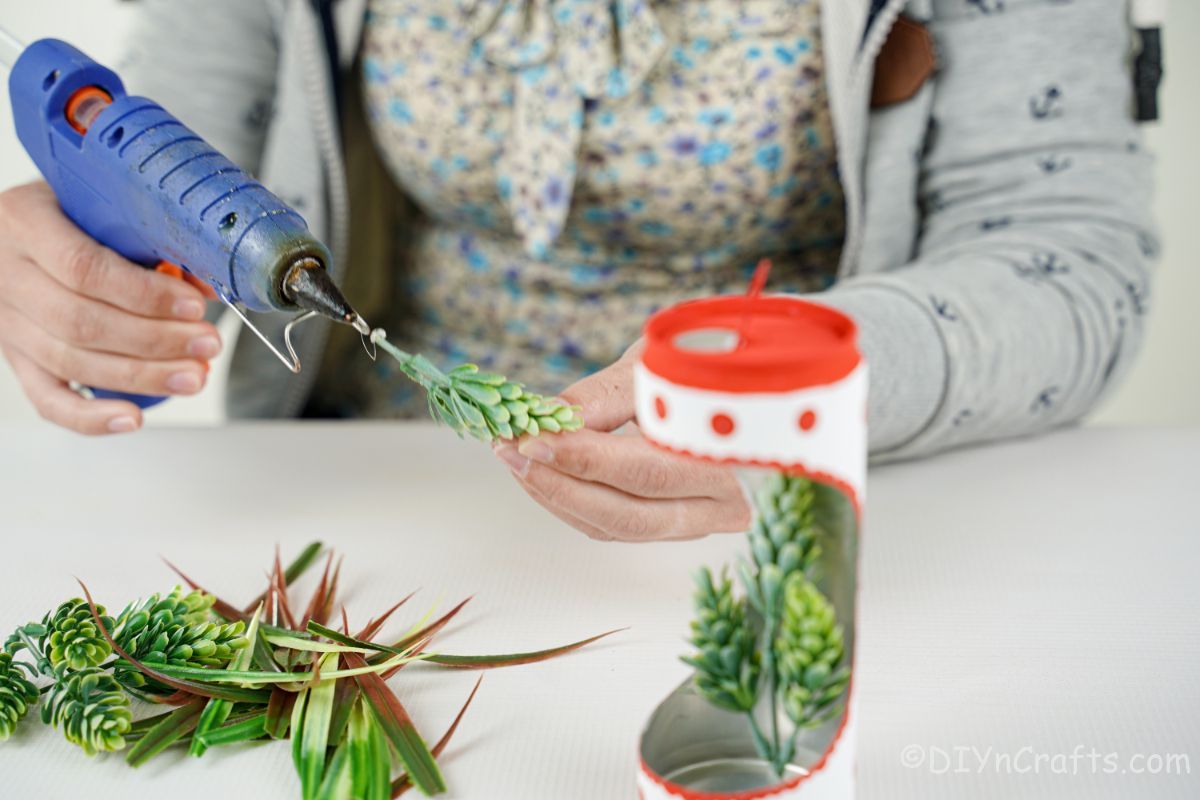 hand gluing fake succulents into soda can planter