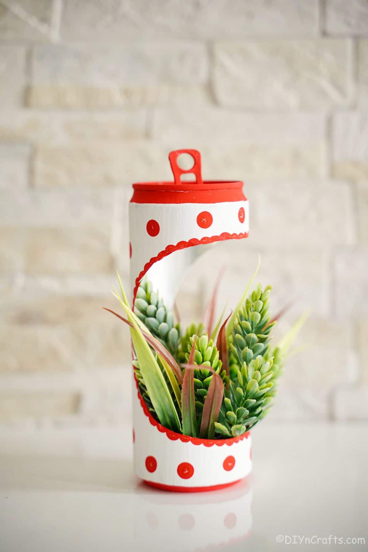 soda can planter with fake succulents on white table with cream brick wall in the background