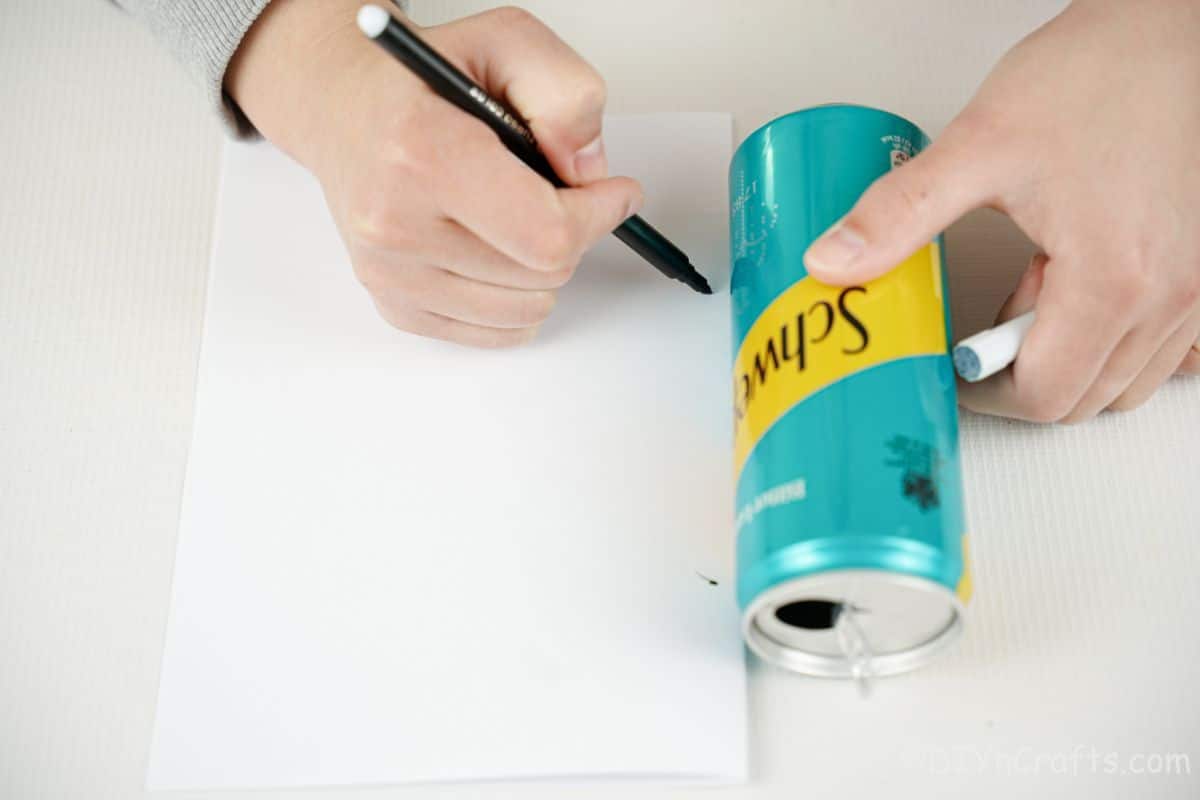 hand tracing shape on white paper next to blue and yellow soda can