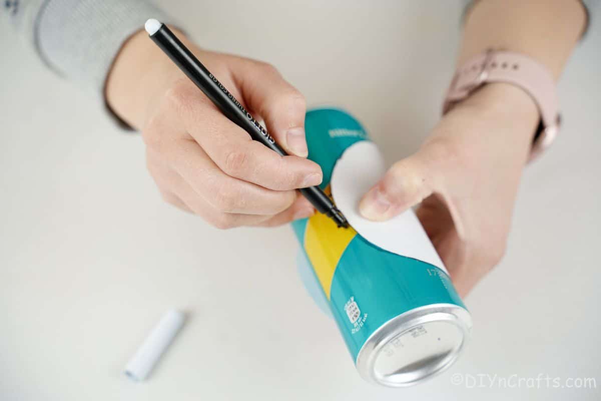 hand tracing onto soda can with black marker