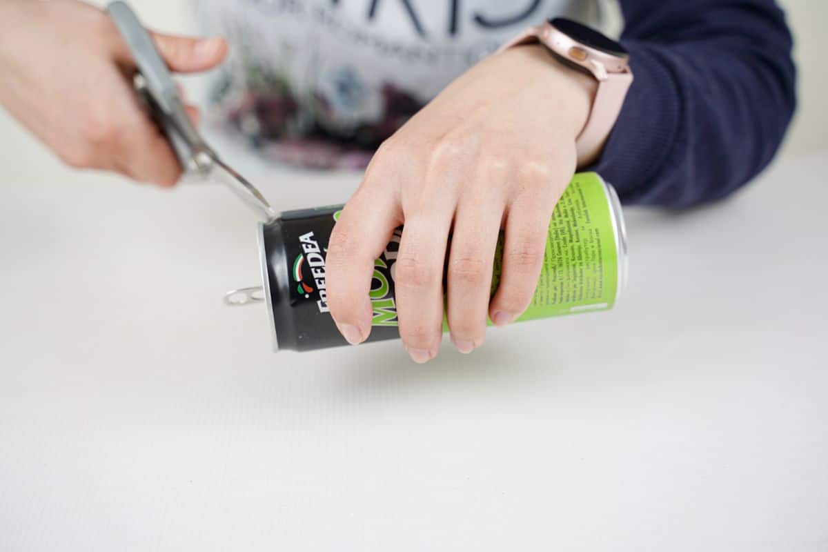 hand holding soda can while scissors cut end off