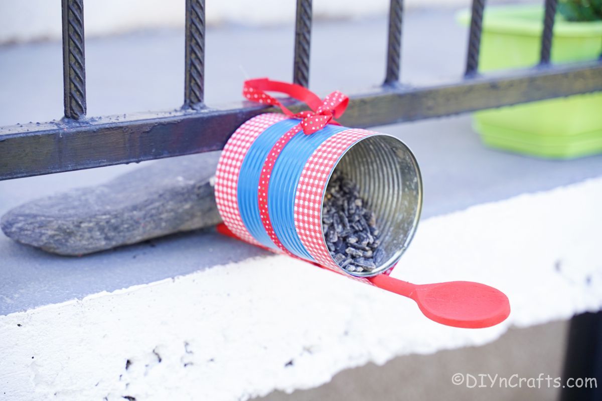 tin can bird feeder propped against porch railing