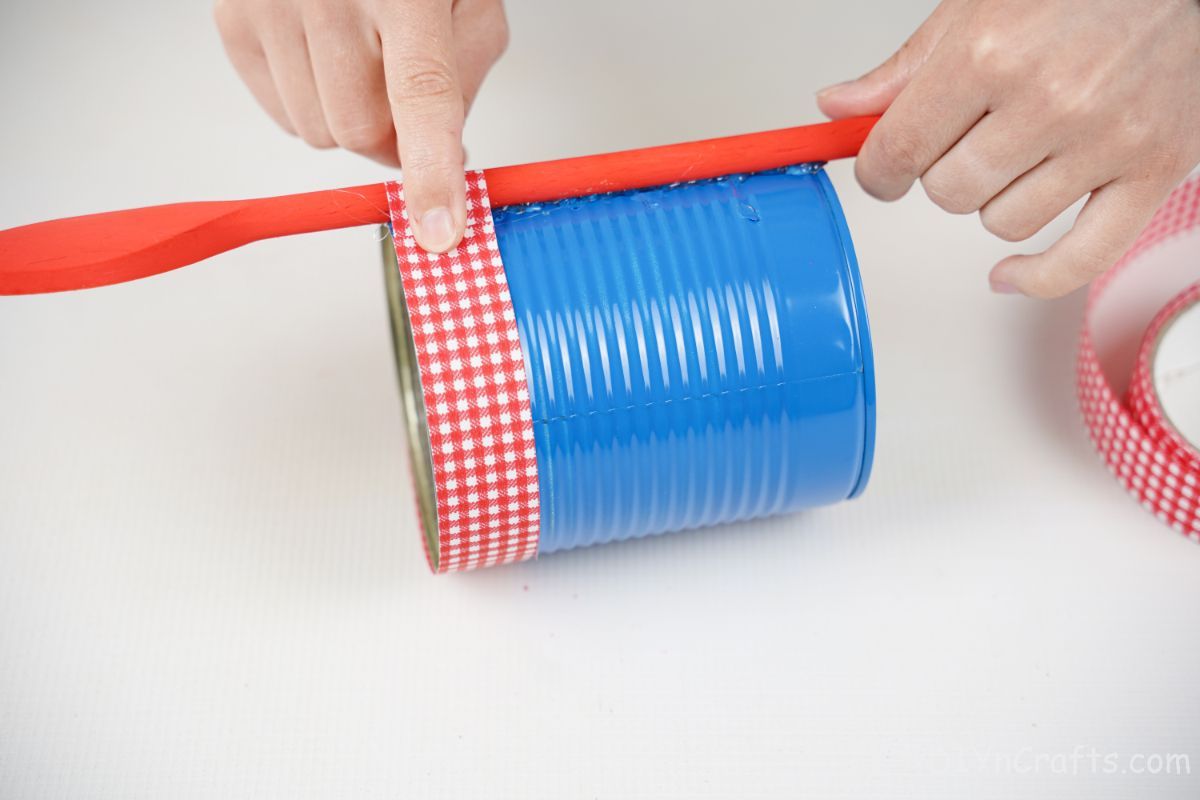 gluing red checked ribbon over red spoon on blue can