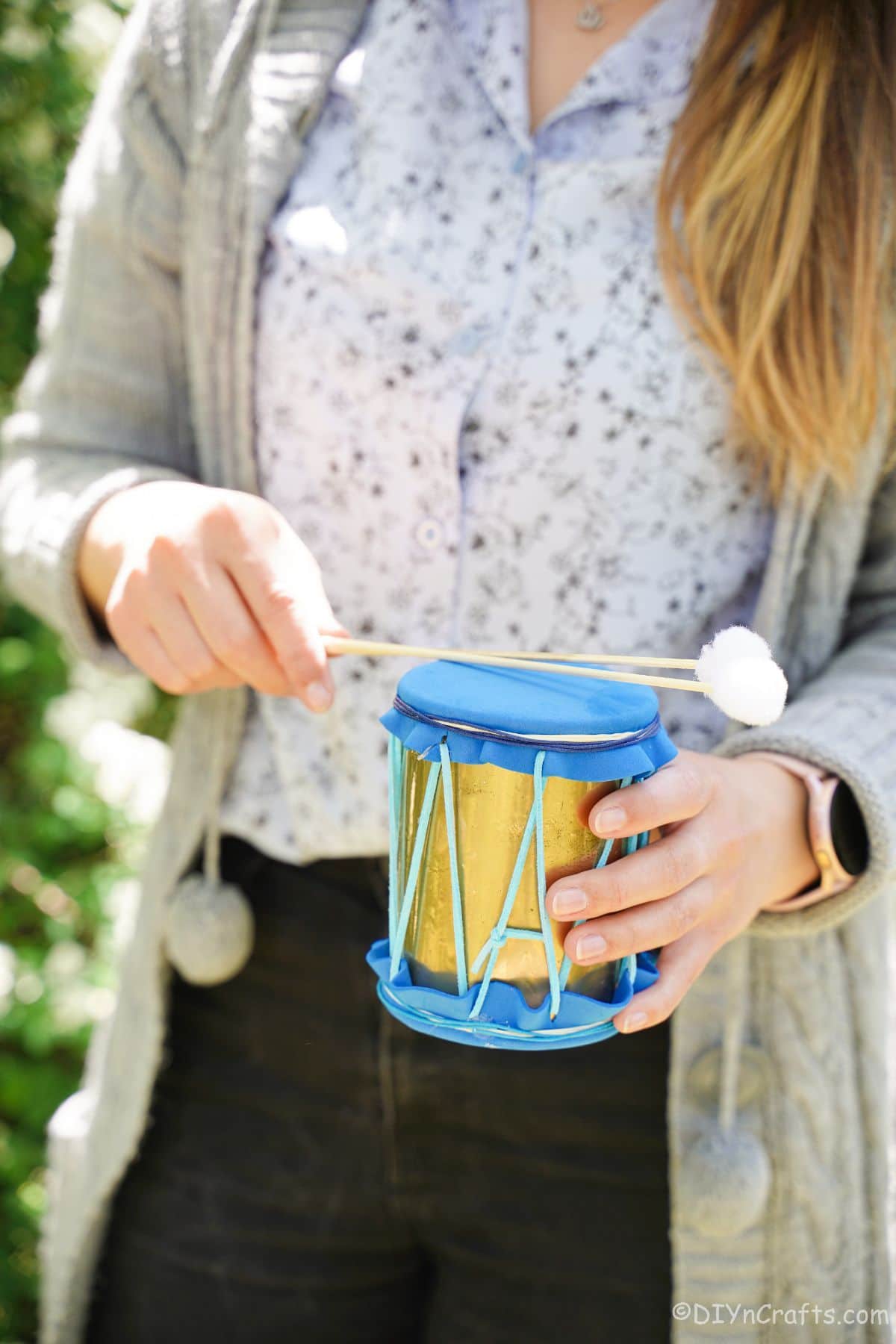 tin can drum with gold and blue accents being held by woman in black pants