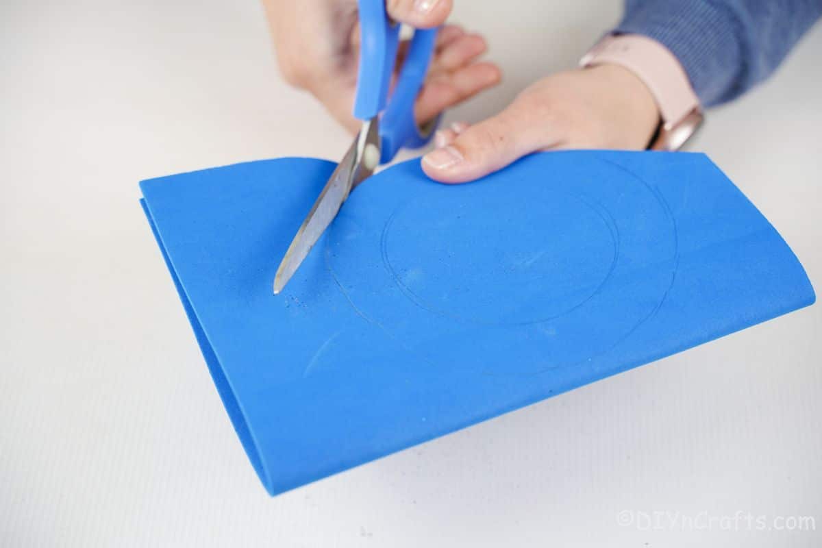 hand holding blue scissors cutting blue foam paper circle