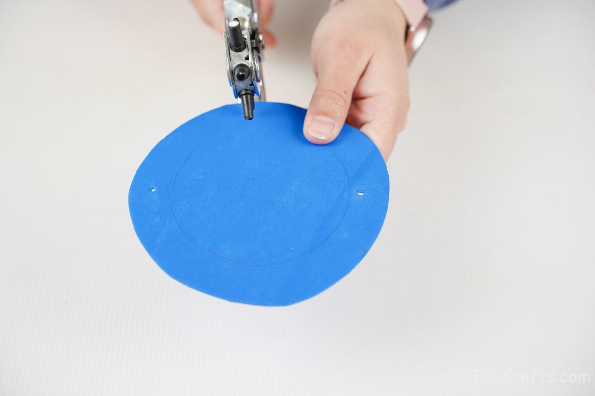 blue foam paper circle being cut with hole punch