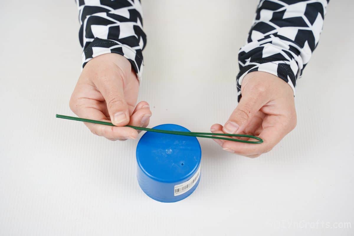 hand wrapping green wire around blue paint can cap