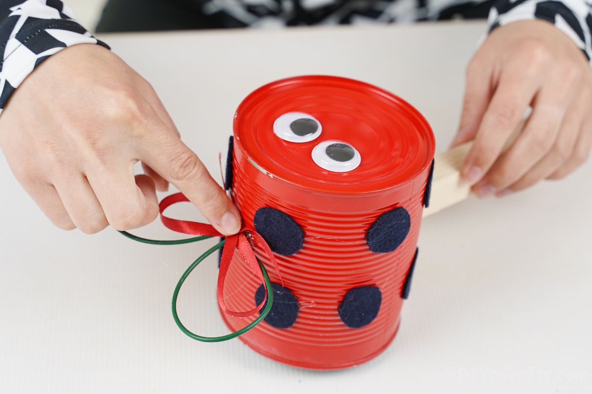 hand gluing bow on top of ladybug tin can