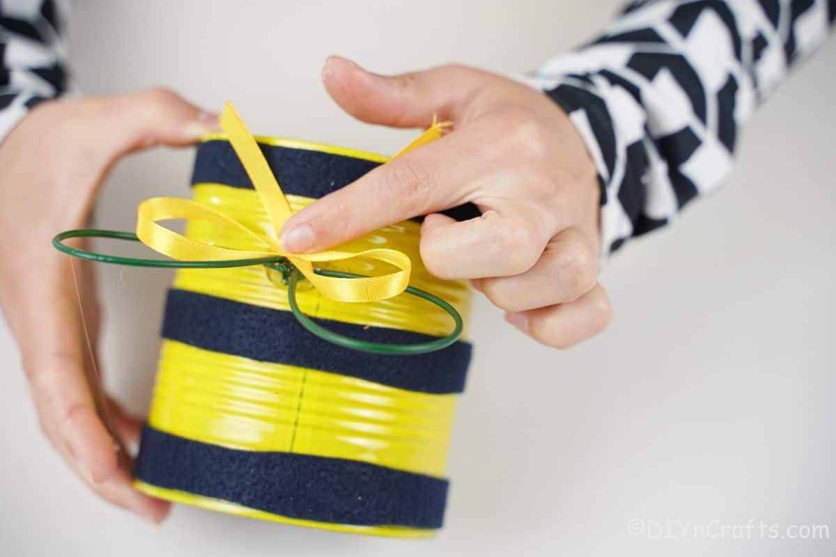 hand tying yellow ribbon on top of tin can bee