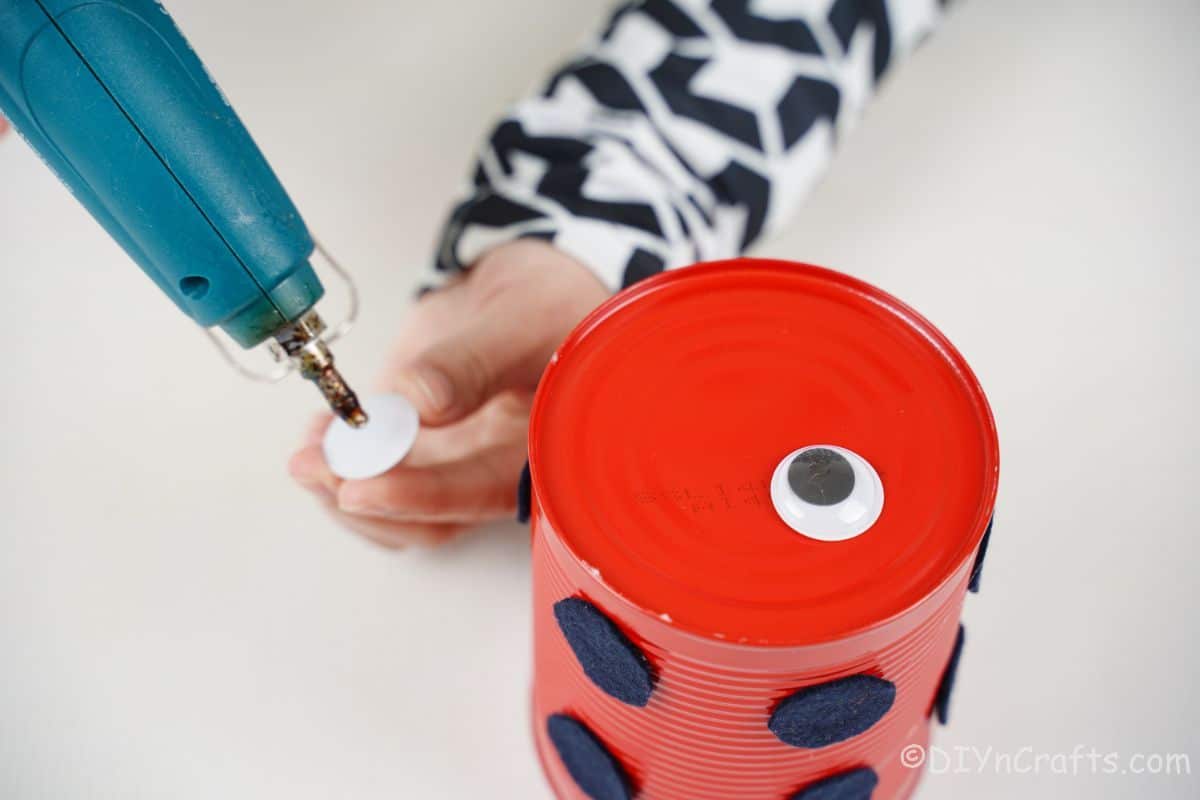hand adding glue to googly eye for tin can