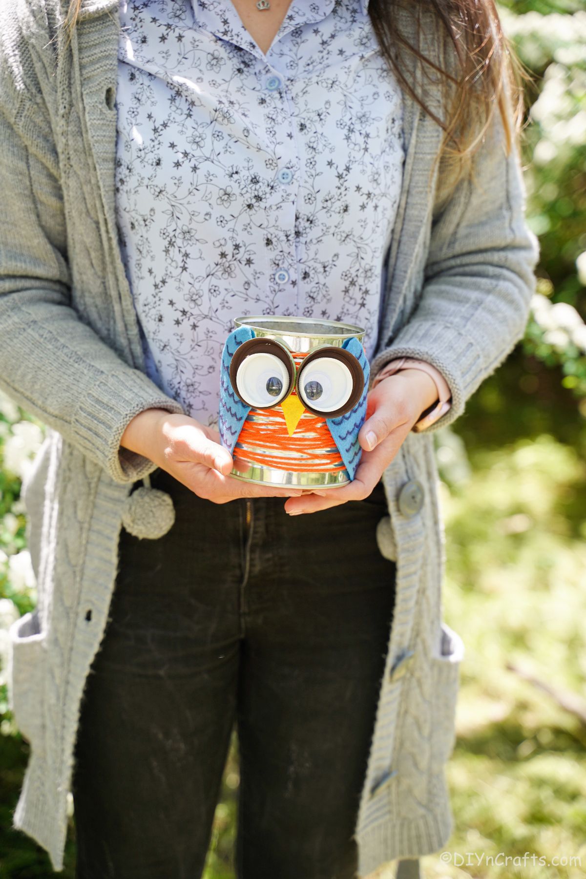 woman in gray sweater holding tin can owl