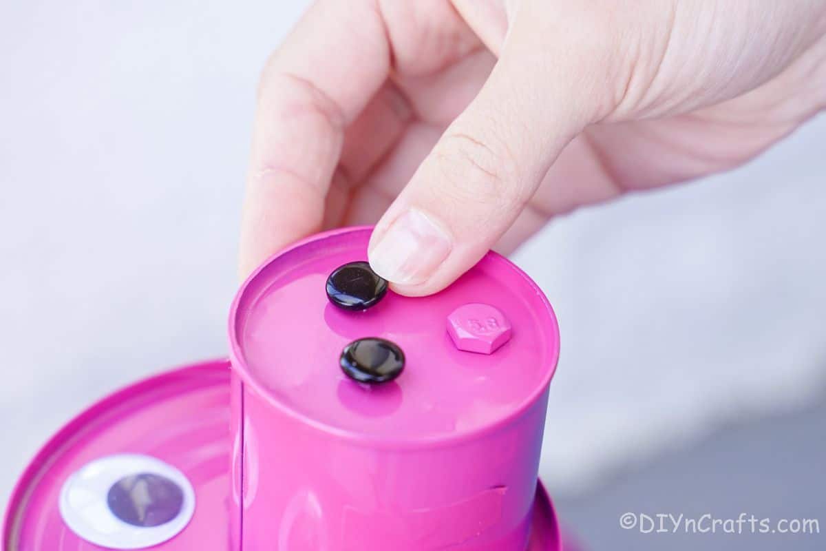 hand putting black buttons on tin can pig