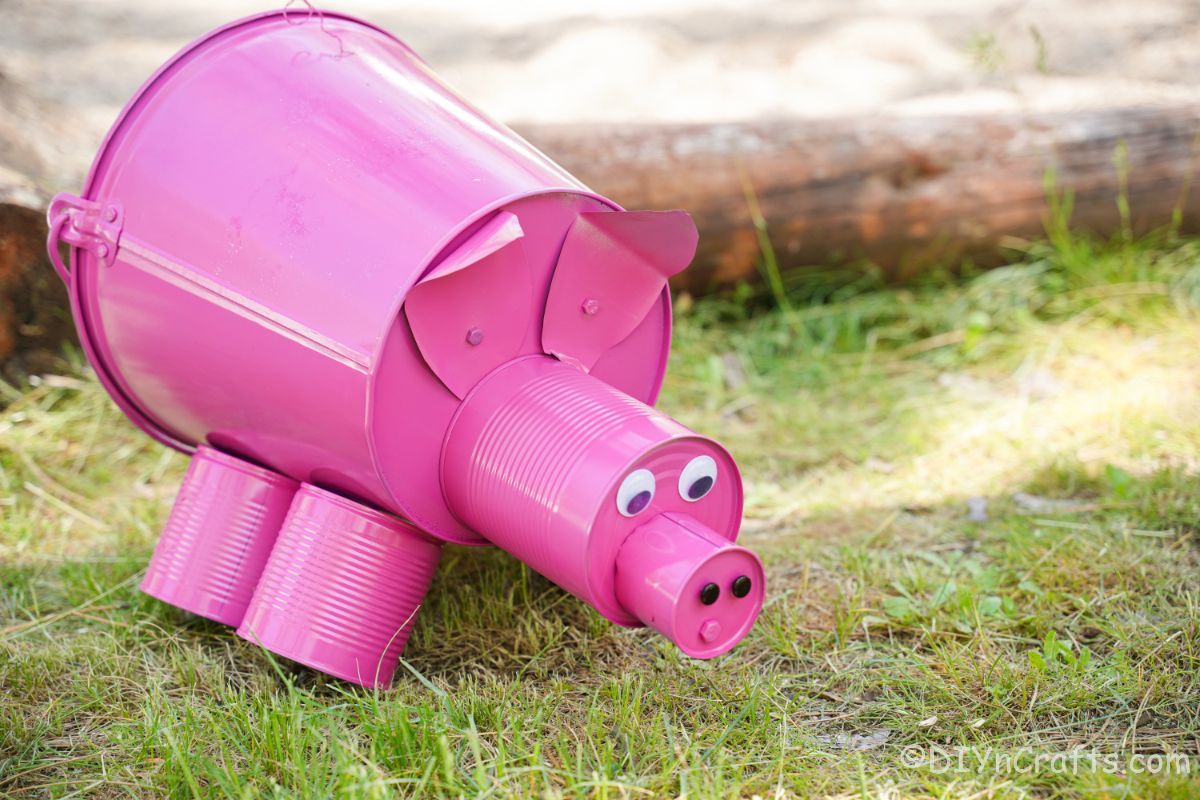 metal pink pig on grass by log